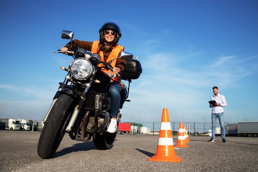 Persona con chaleco naranja y casco sobre motocicleta, persona al fondo.